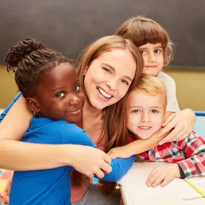 Preschool teacher hugging students in the Grasshoppers classroom